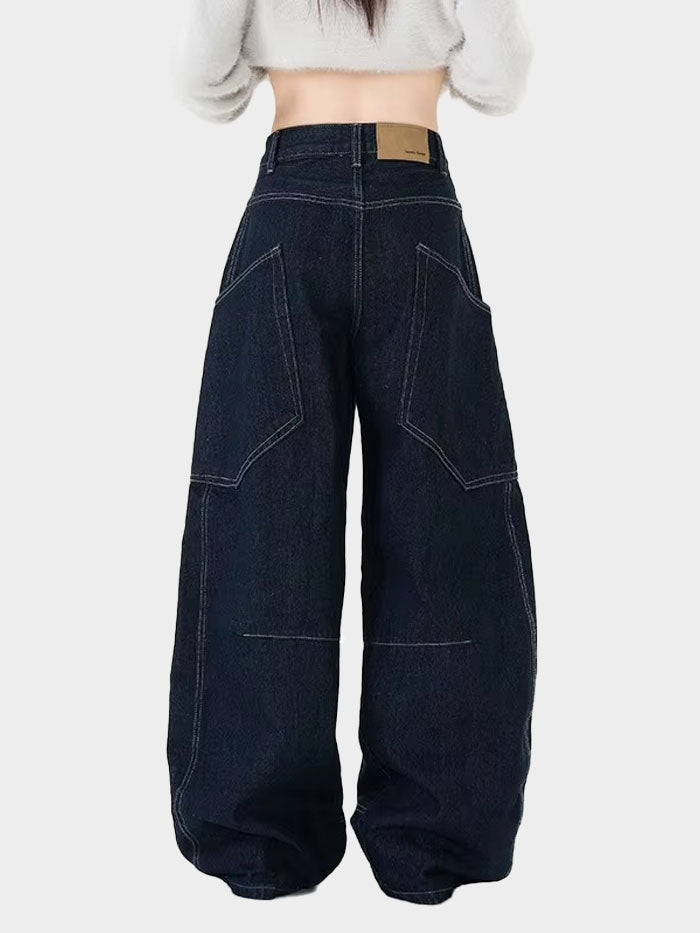 Back view of oversized dark wash jeans featuring large patch pockets and bold curved stitch details.