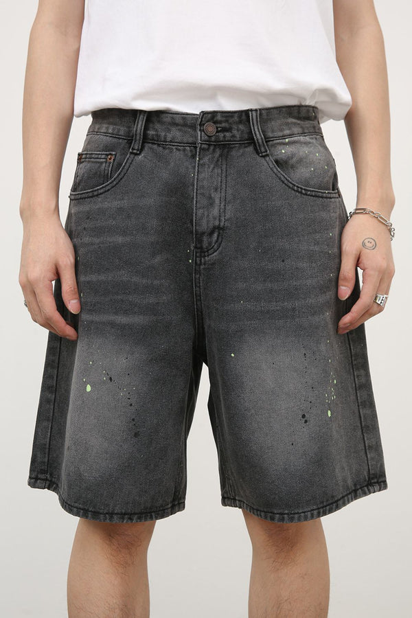 Front view of black denim shorts with neon green paint splatter details, styled with white tee and sneakers