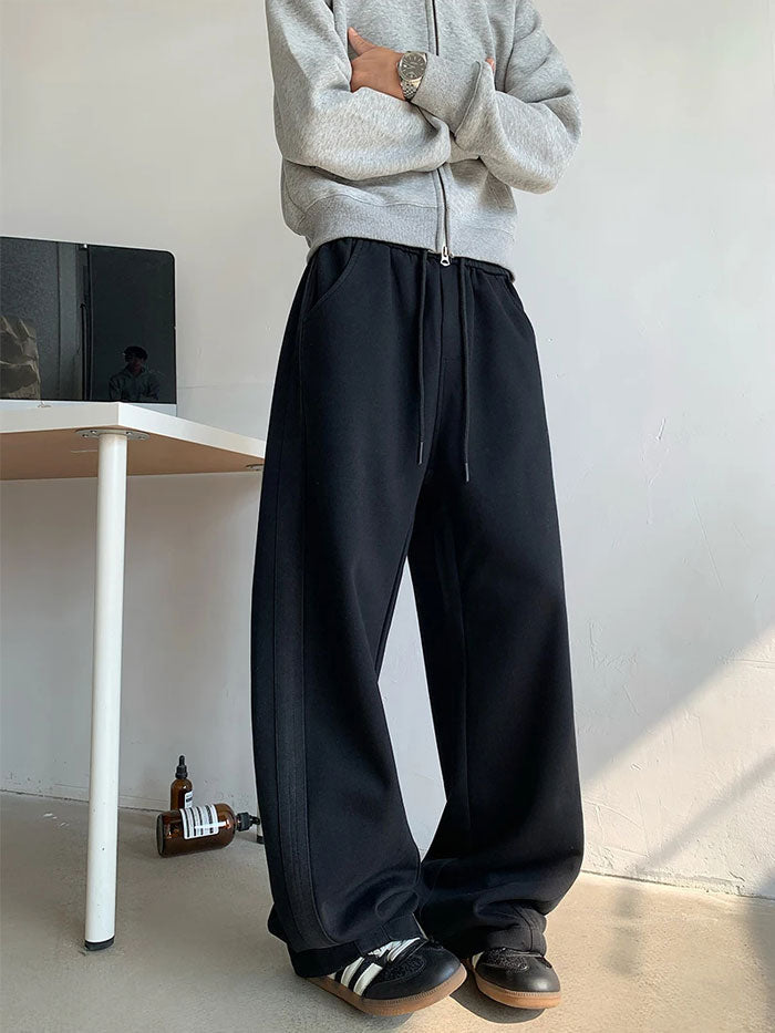 Side view of men’s oversized black sweatpants with relaxed street fit.