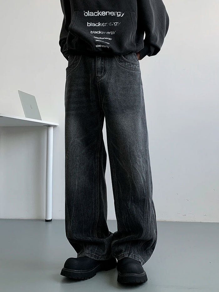 Man wearing black washed wide-leg baggy jeans with chunky black shoes, seated on a white chair.