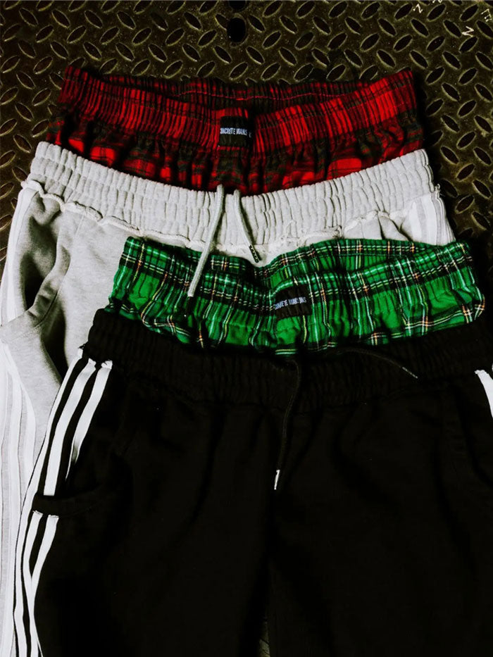 Close-up lifestyle shot of Concrete Mans track pants highlighting the layered red and green plaid waistbands.