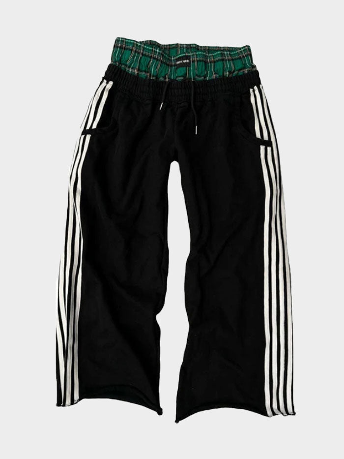 Black track pants with white stripes and green plaid waistband detail by Concrete Mans, laid flat.