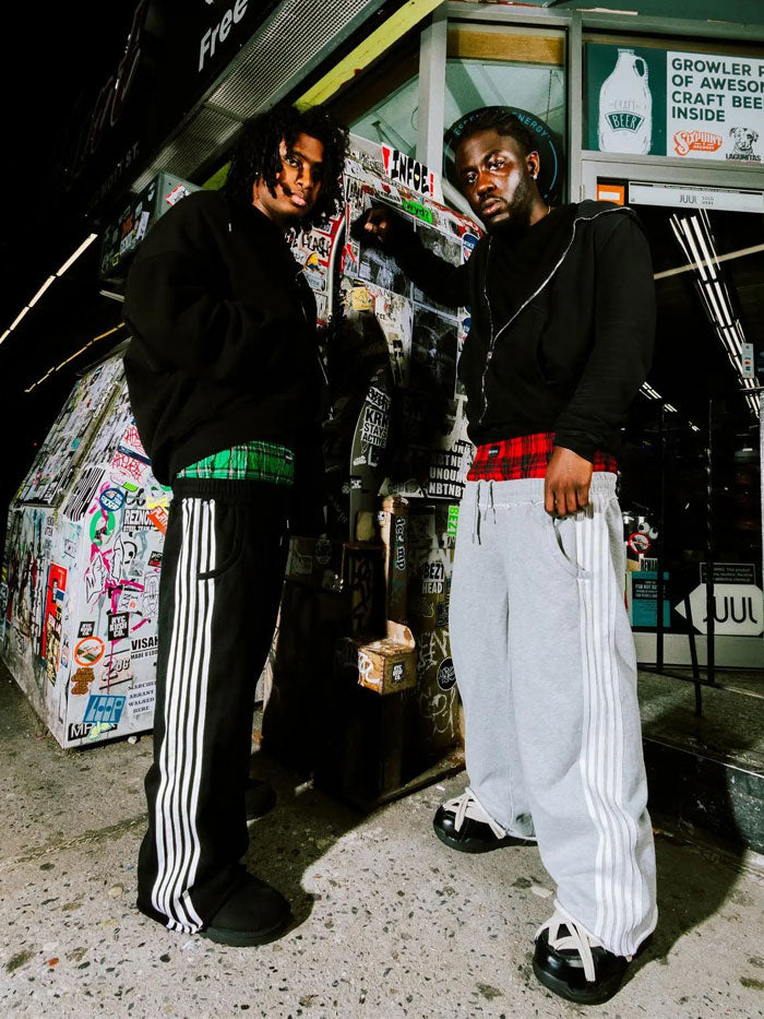 Flatlay of Concrete Mans track pants collection in black and grey with plaid waistband layers.