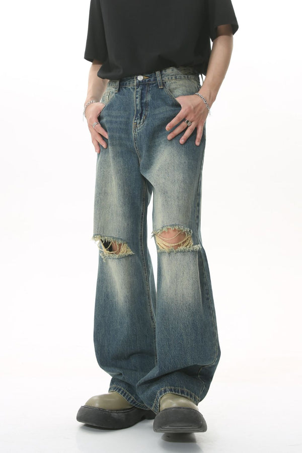 Front view of distressed vintage wide-leg jeans in faded blue wash with knee rips.