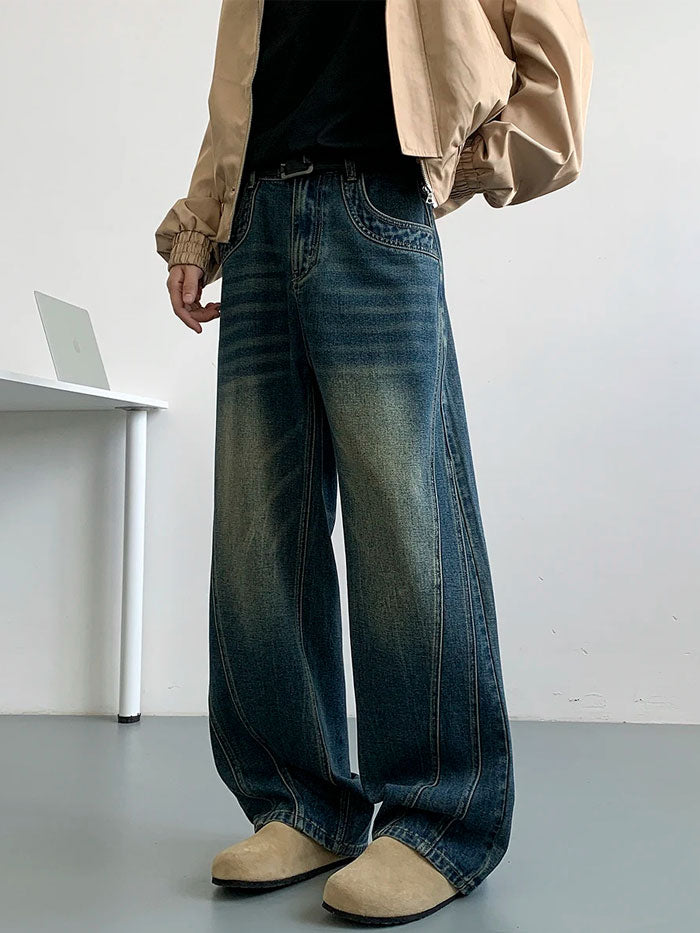 Front view of faded blue baggy jeans paired with a beige bomber jacket and tan suede shoes.