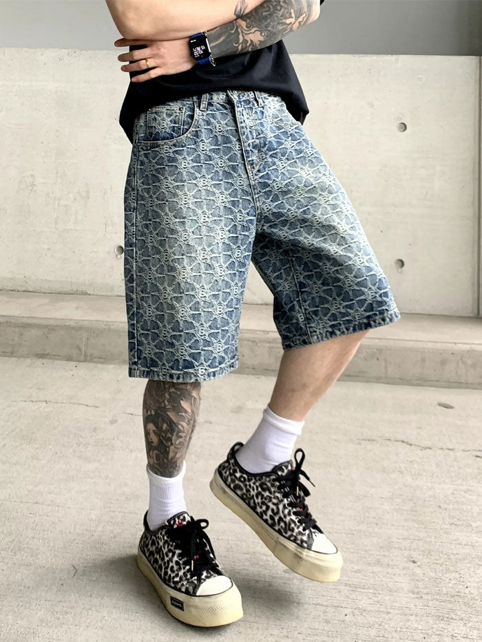 Front view of relaxed-fit men's denim shorts with faded designer monogram pattern.