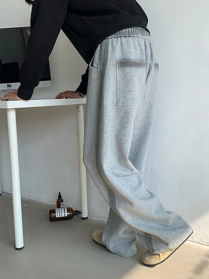 Men’s light grey oversized sweatpants with wide-leg fit, casual leaning pose.