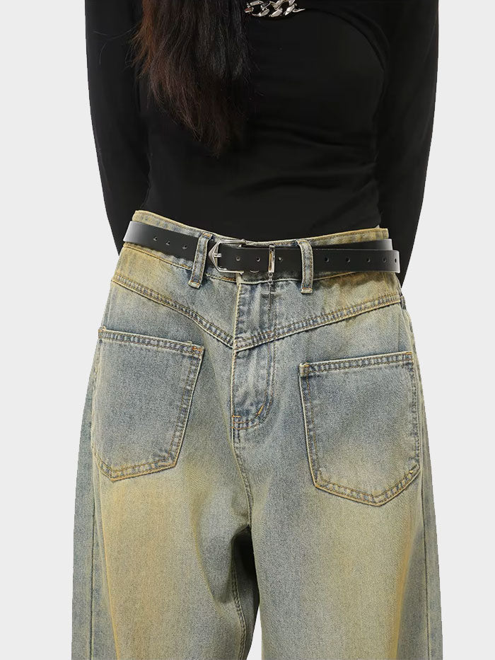 Close-up of black wide-leg jeans featuring a black belt with a cross charm and high waistline.