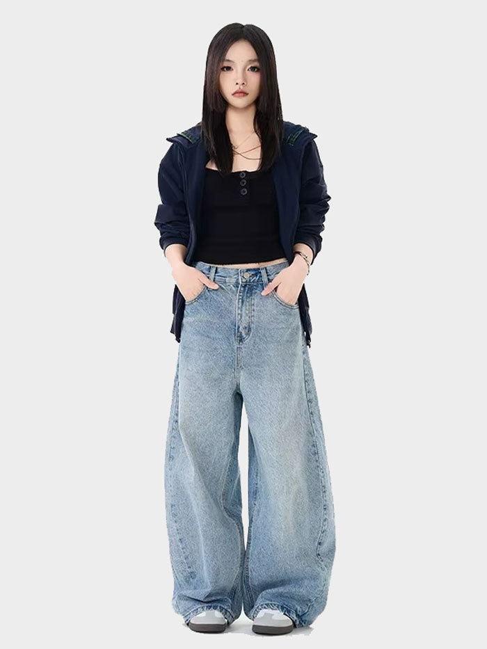 Full-body image of a woman in streetwear style, wearing light blue baggy jeans, a black crop top, and sneakers.
