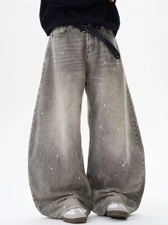Model wearing streetwear outfit with grey paint-splattered baggy jeans and black top.
