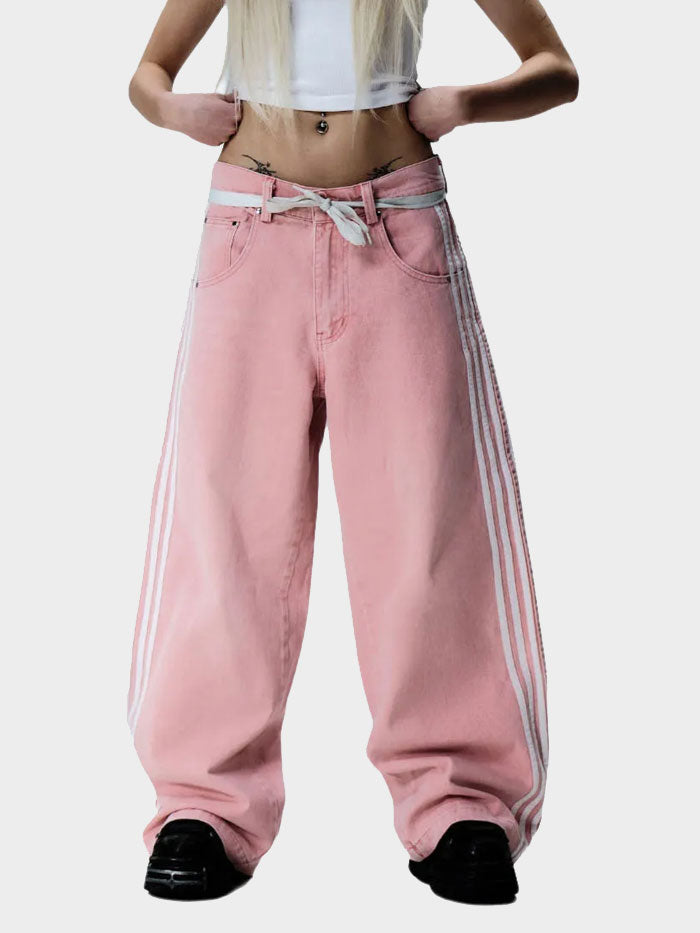 Model wearing pink baggy jeans with white side stripes styled with a white crop top and black shoes.
