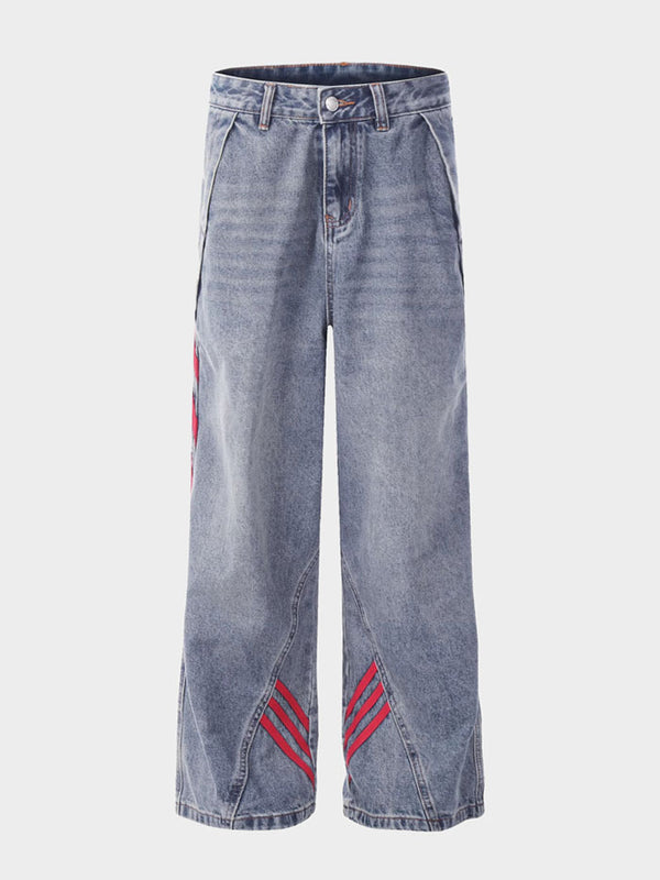 Flat lay of unisex wide-leg jeans with red stripes on faded denim and angular panel detailing.