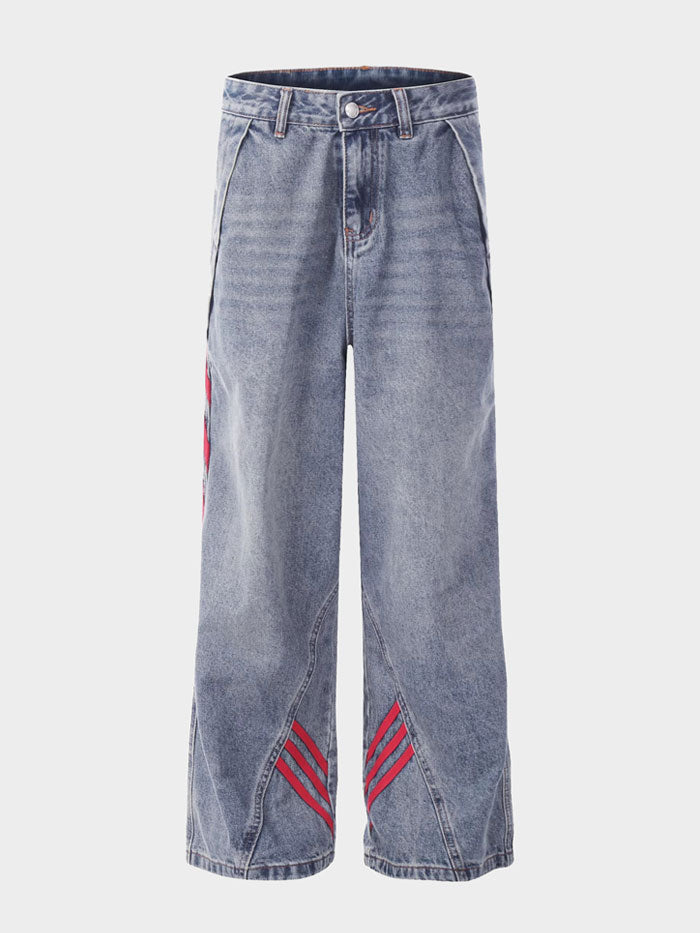 Flat lay of unisex wide-leg jeans with red stripes on faded denim and angular panel detailing.