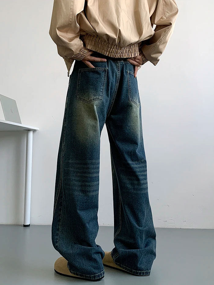 Man in black loose jeans and black hoodie with graphic print, standing indoors near white desk.