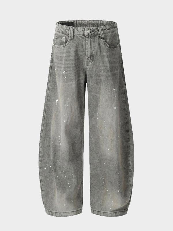 Close-up view of grey baggy jeans with white paint splatter details on denim fabric.
