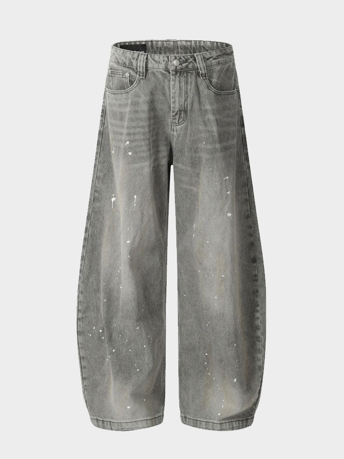 Close-up view of grey baggy jeans with white paint splatter details on denim fabric.