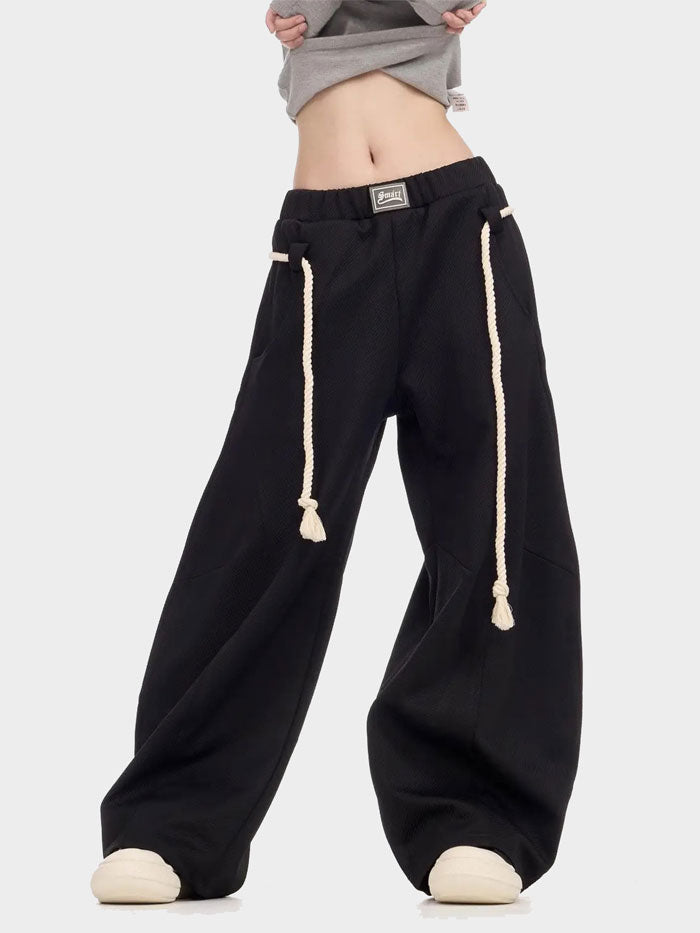 Street-style black wide-leg track pants with exaggerated drawstring details.