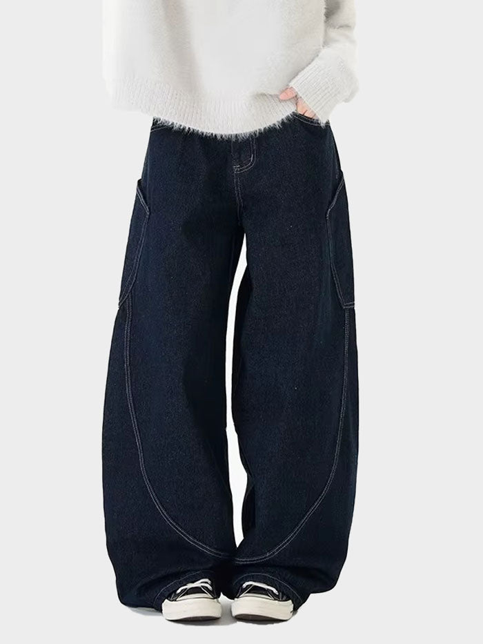 Streetwear-inspired dark denim jeans with curved seams, styled in a relaxed pose with a cozy knit top.